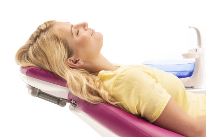 En glad patient læner sig tilfreds tilbage og hviler hovedet på nakkestøtten af patientstolen på en tandlægeunit